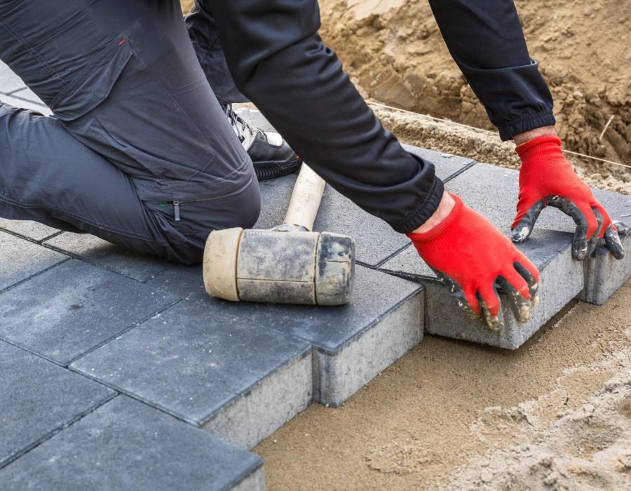 Hands of worker installing concrete paver blocks with rubber hammer